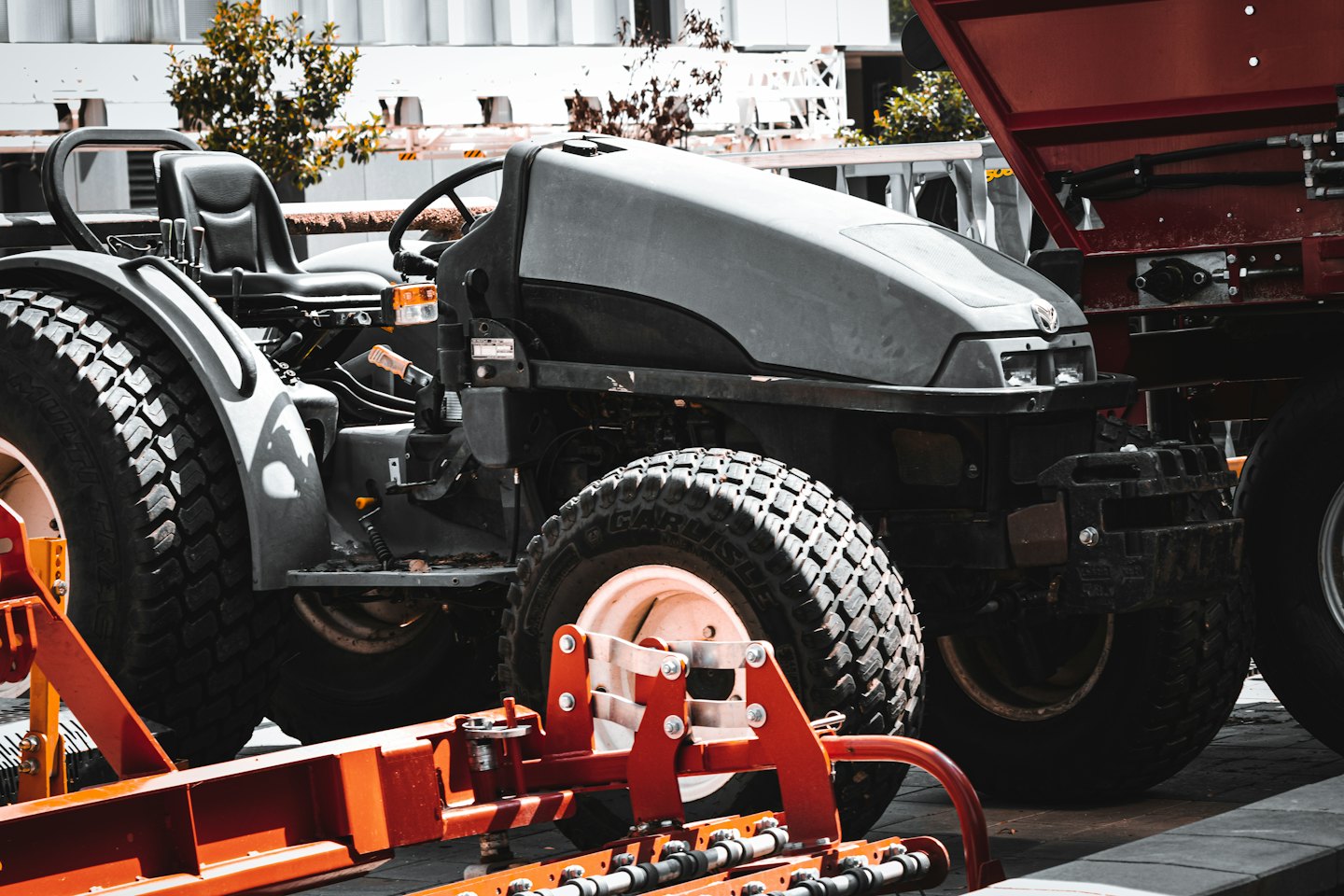 Grauer Kompakttraktor mit einem leuchtend orangefarbenen Landwirtschaftsgerät.