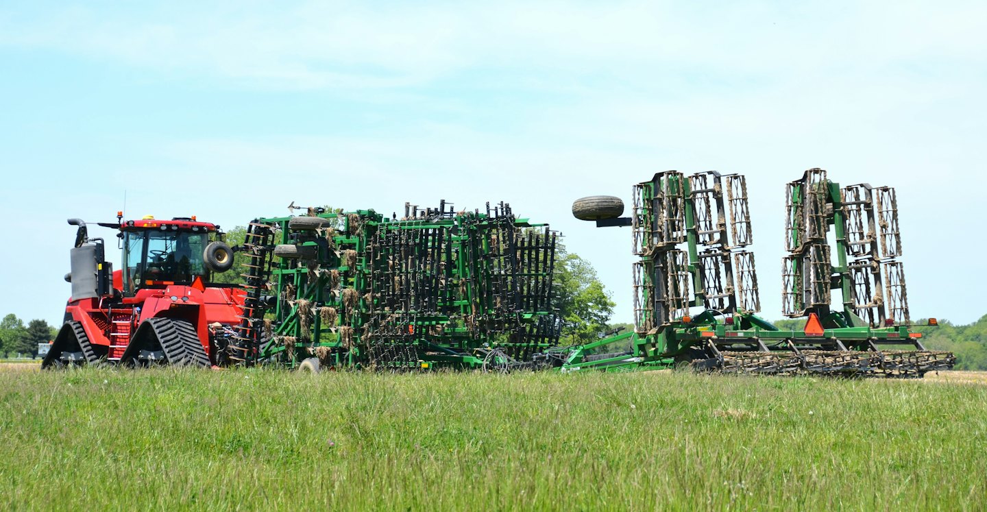 Roter Traktor zieht ein großes Landwirtschaftsgerät durch ein Feld.
