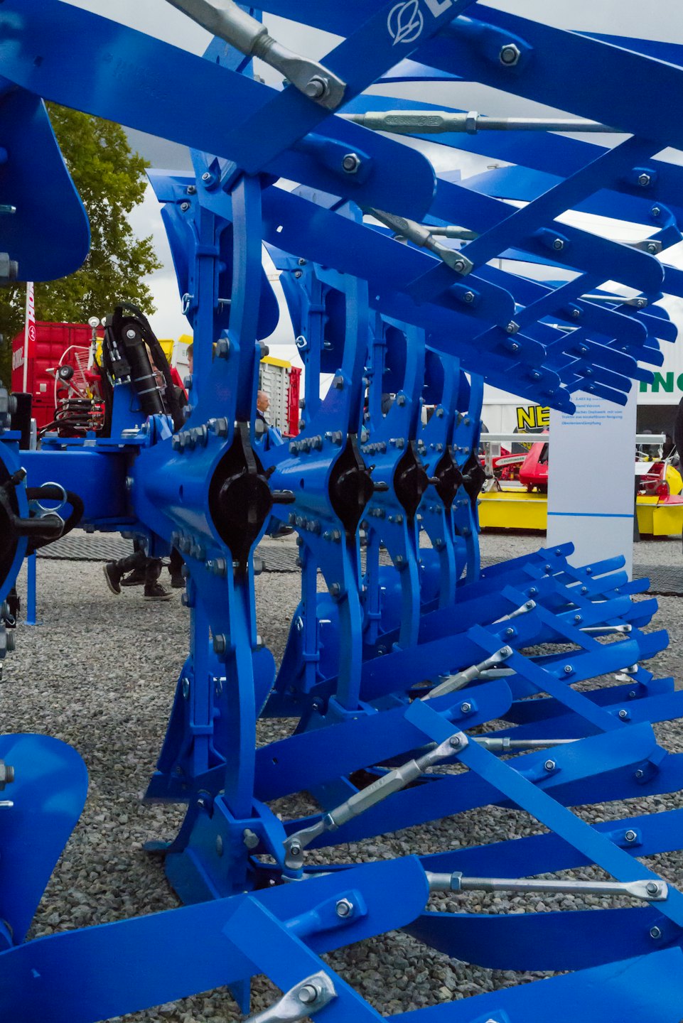 Leuchtend blauer Landwirtschaftsgrubber mit schrägen Metallzinken auf Schotter.