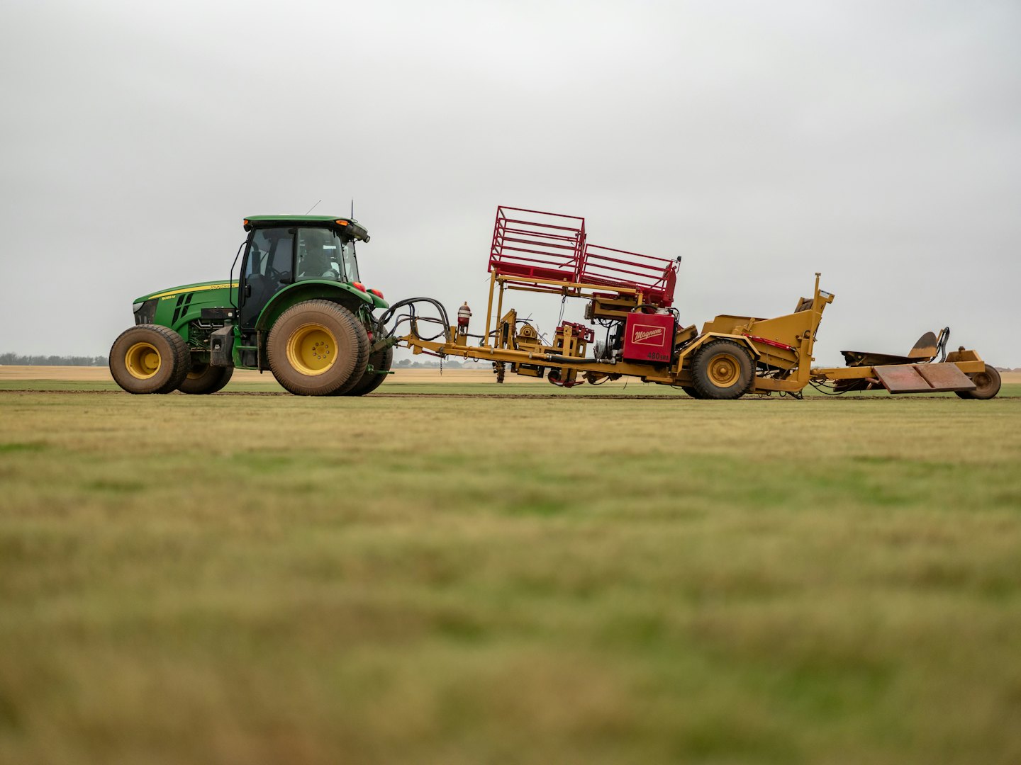 Grüner Traktor zieht einen gelb-roten Rasenmäher über ein Feld.
