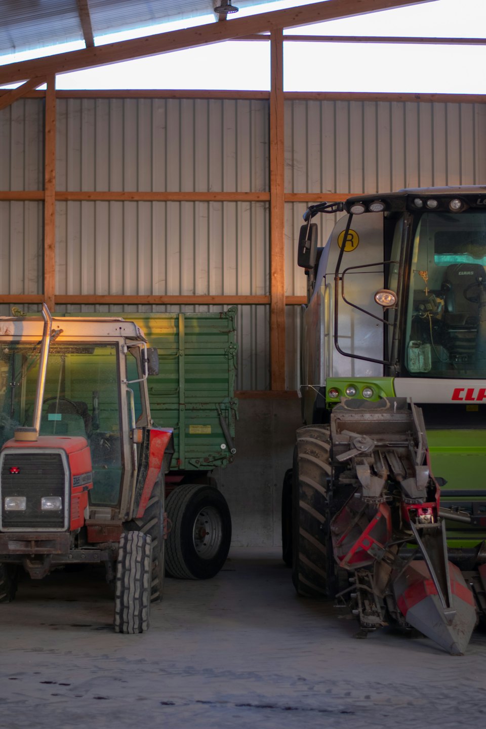 Roter Traktor und grüner Mähdrescher parken in einer Scheune.