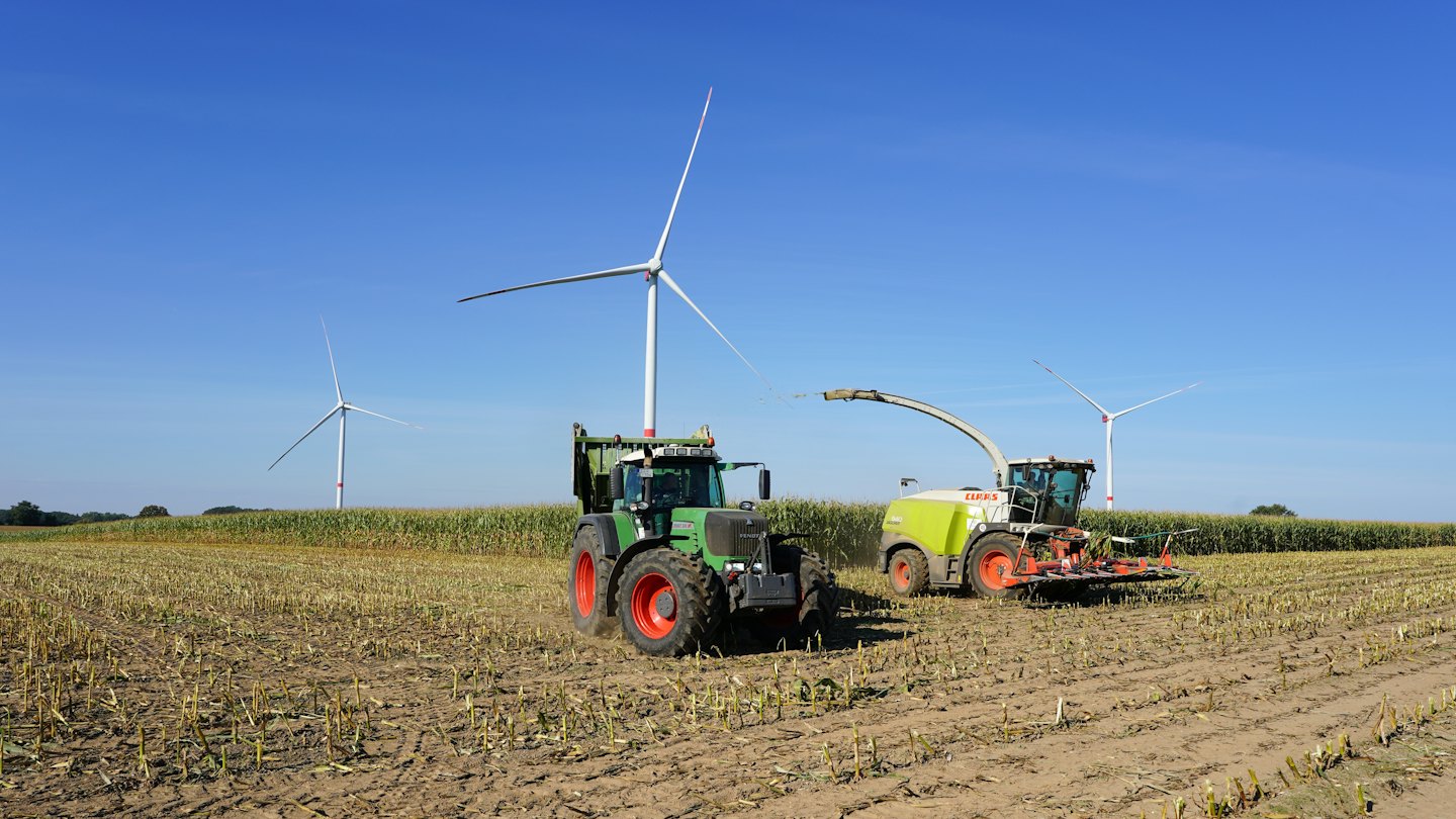 Landwirtschaftliche Maschinen ernten Mais in der Nähe von Windrädern auf einem Feld.